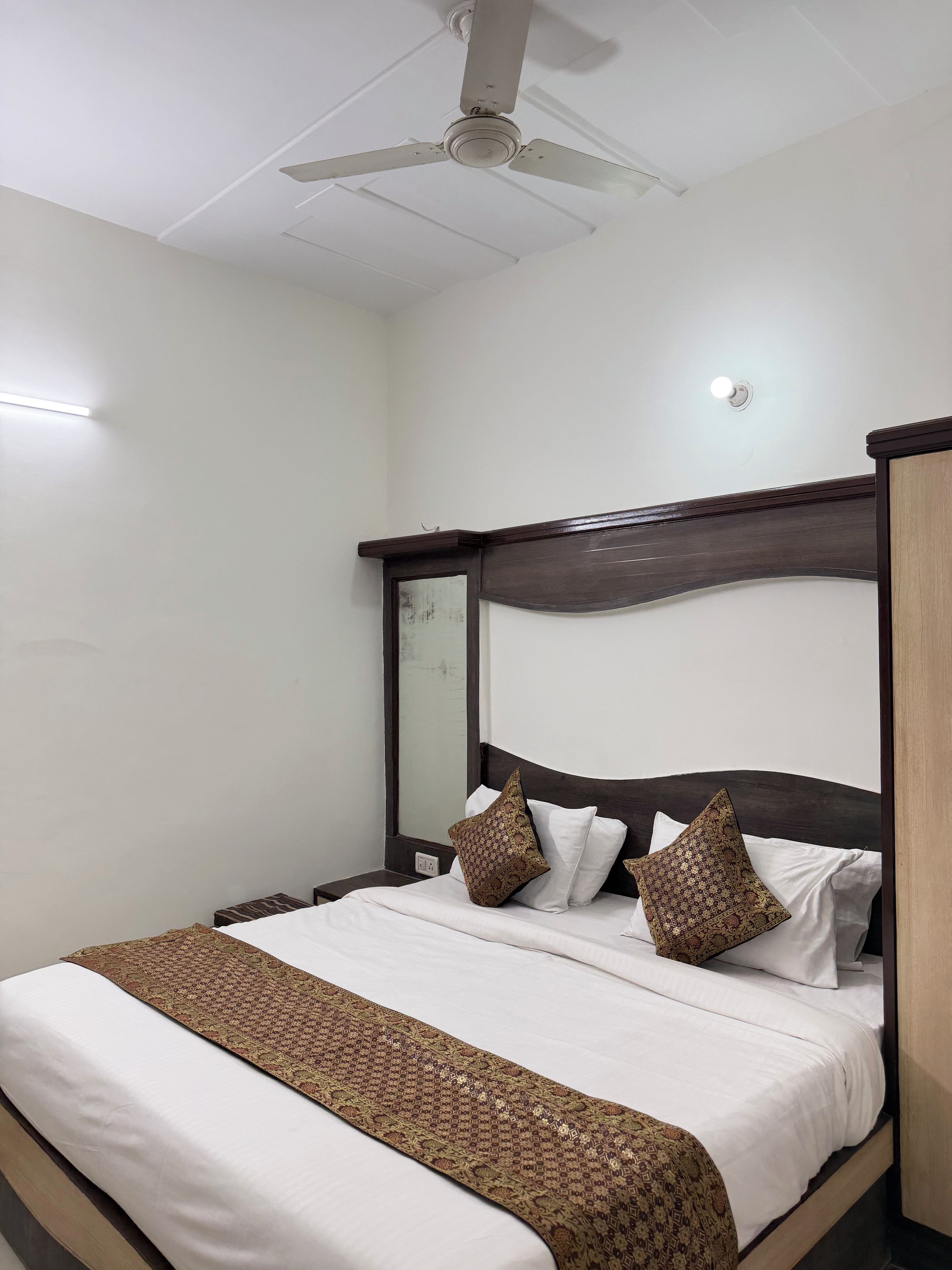 Een hotelkamer met een bed, een plafondventilator, een nachtkastje en een bijzettafeltje.