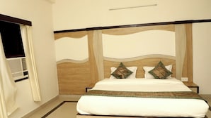 A neatly made bed with a wooden headboard, white bedding, and decorative pillows. - Hotel The Golden Bird (Agra)