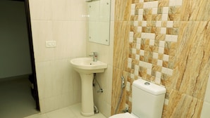 A bathroom with a pedestal sink, a toilet, and a shower area with a tiled wall. - Hotel The Golden Bird (Agra)