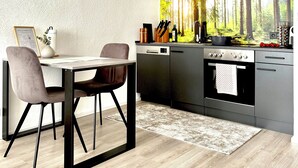 A modern kitchen with a dining area, featuring a built-in oven, dishwasher, and a large window with a forest view.