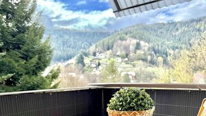 A wooden table and chairs on a balcony with a view of a forested valley.