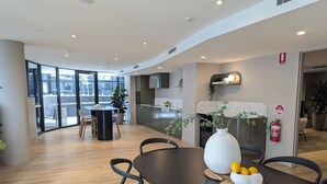 Un comedor moderno con una mesa de madera oscura, sillas negras y un jarrón blanco con limones.