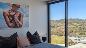 Un dormitorio con una cama grande, vista a un paisaje a través de una ventana y un cuadro en la pared.