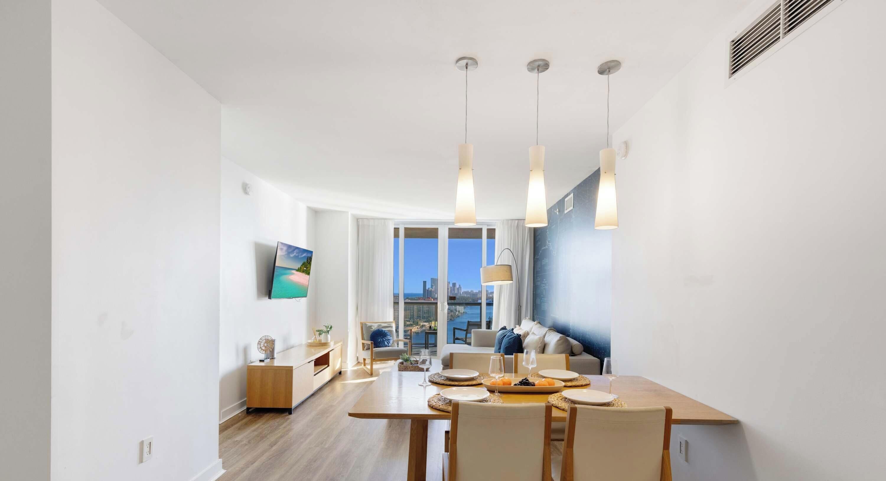 A modern dining area with a wooden table, chairs, and a city view through large windows.