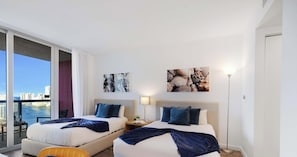 Quarto de hotel com duas camas, varanda e vista para a cidade, além de obras de arte nas paredes.