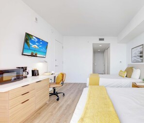 Habitación de hotel con escritorio, silla, dos camas, televisor y puerta que da a otra habitación.