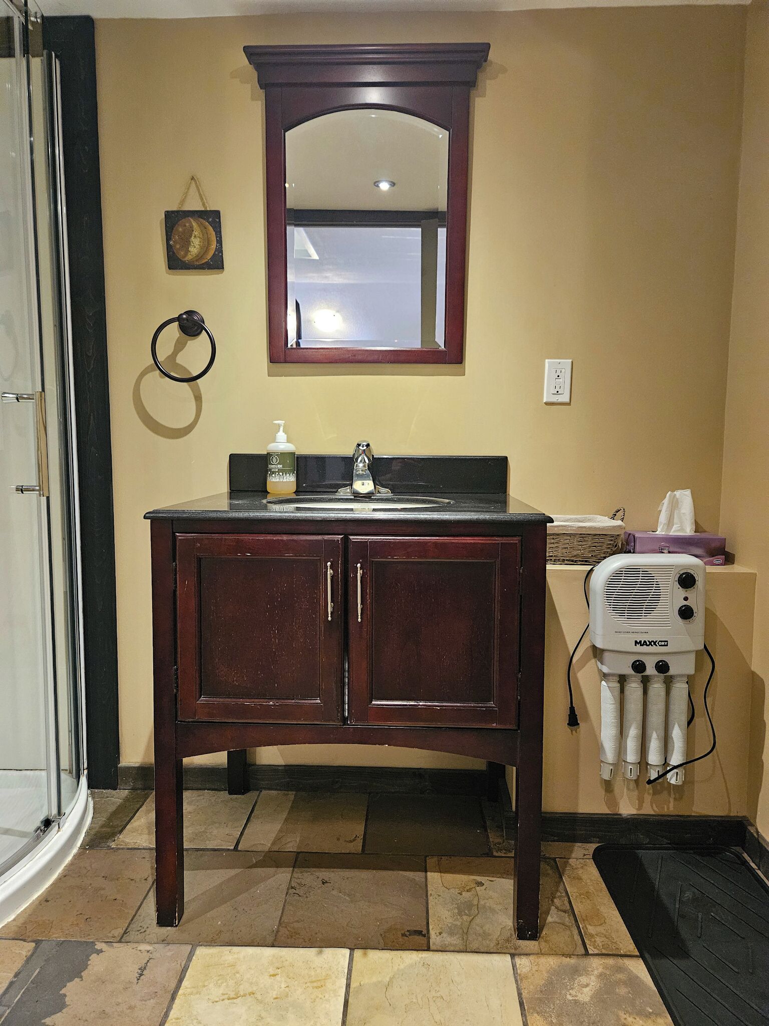 Une salle de bain avec un meuble-lavabo en bois, un miroir, un porte-serviettes, un distributeur de savon et un ventilateur MAXX.
