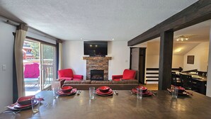 Ein Wohnzimmer mit Kamin, zwei rote Sessel, eine Couch und ein Essbereich mit Tisch für vier Personen.