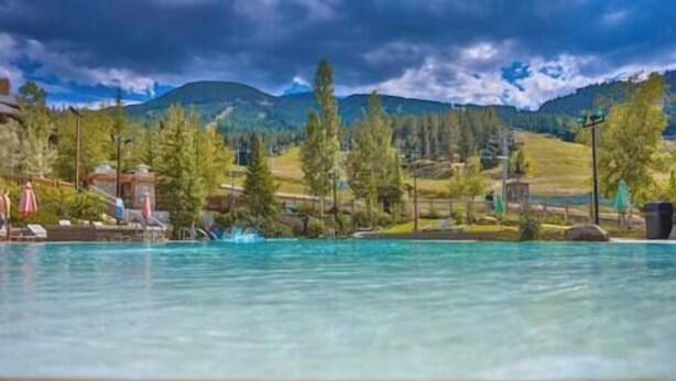 Ein Schwimmbad mit klarem Wasser, umgeben von Bäumen und einer Berglandschaft.