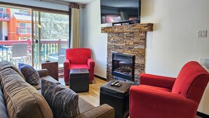 Ein Wohnzimmer mit Kamin aus Stein, einem roten Sessel, einer Couch und einem Fernseher, der über dem Kamin angebracht ist.