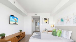 Un dormitorio con cama, televisión, escritorio, lámpara y obras de arte en las paredes.