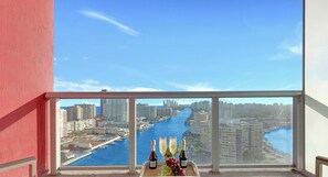 A balcony with a table set for two, overlooking a cityscape and a river.