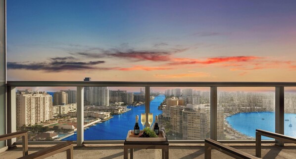 A balcony with a cityscape view, a table with bottles and glasses, and a railing.