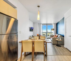 A modern kitchen with a refrigerator, dining table, chairs, and a TV mounted on the wall.