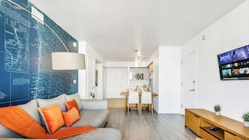 Ein modernes Wohnzimmer mit einer großen Karte an der Wand, einem Sofa mit orangen Kissen, einem Essbereich und einem Fernseher, der einen Film zeigt.