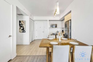 A modern kitchen with white cabinets, a wooden dining table, and a hanging light fixture.