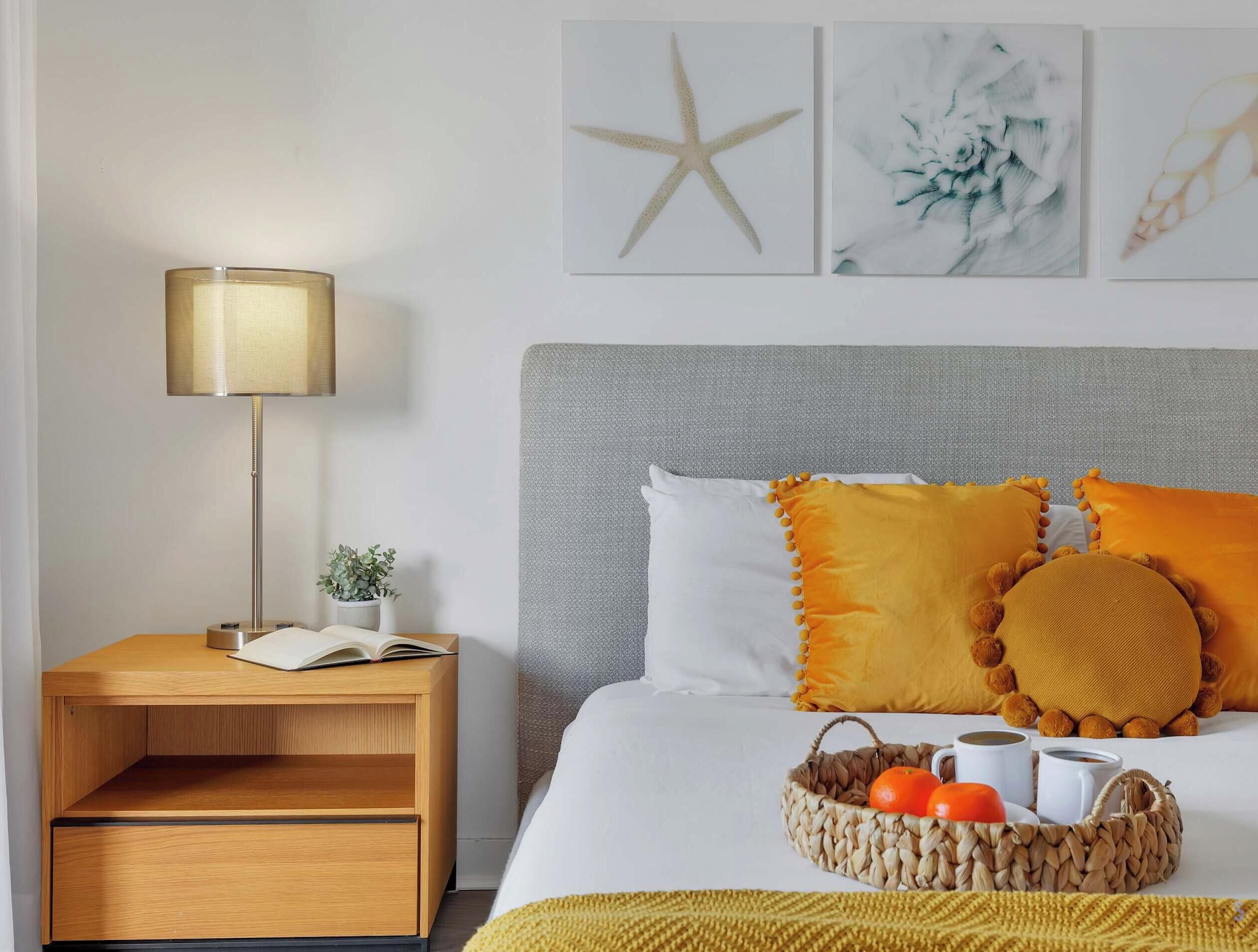 A neatly arranged bedroom with a bed, bedside table, lamp, and wall art.