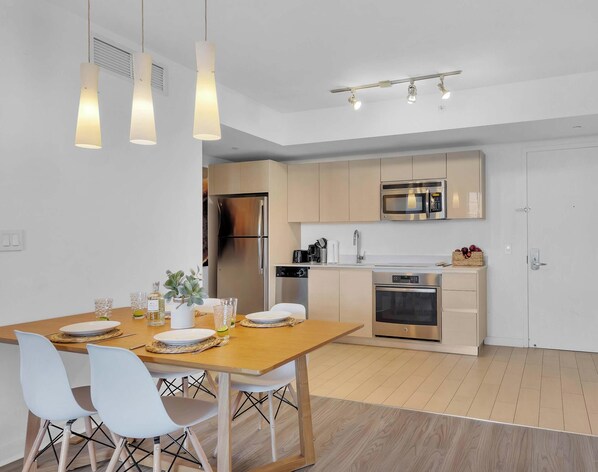 A modern kitchen with a refrigerator, microwave, oven, and dining area with a table set for two. - Spectacular 2BR Apt w/ Private Balcony + Pool (Hallandale Beach)