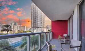 A balcony with a city view, a red wall, and a table with chairs.