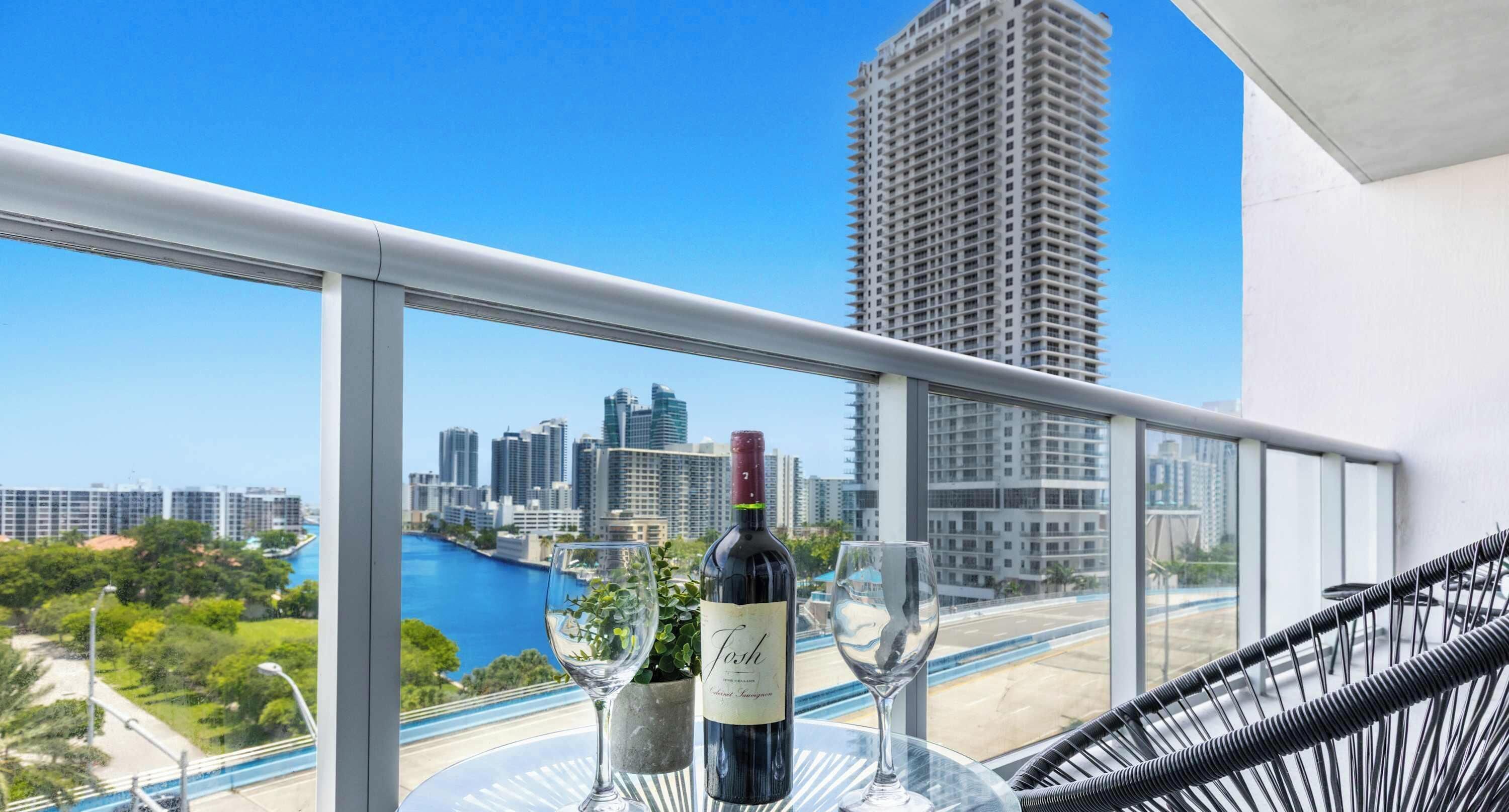 Un balcon avec vue sur la ville, une bouteille de vin et deux verres posés sur une table.