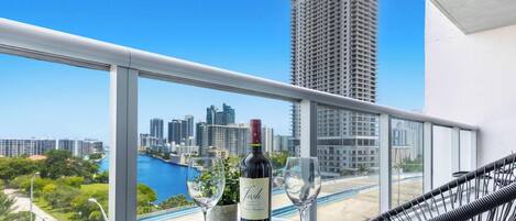 A balcony with a city view, a bottle of wine, and two glasses on a table.