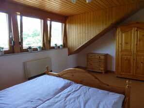 Une chambre avec un plafond en bois, un lit, une commode et une fenêtre ornée de plantes.