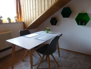 Une pièce avec une table blanche, deux chaises, une plante verte et des étagères vertes hexagonales accrochées au mur.