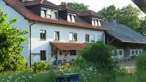 Ein zweistöckiges Haus mit rotem Ziegeldach, zahlreichen Fenstern und einer Veranda.