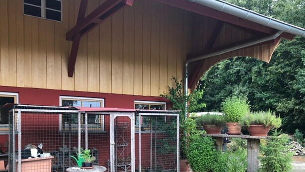 Ein hölzernes Gebäude mit einem eingezäunten Bereich, der zwei Vogelkäfige mit Pflanzen enthält.