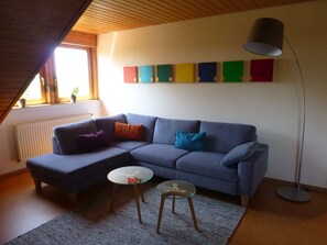 A modern living room with a sectional sofa, two glass tables, a floor lamp, and a colorful wall art piece.