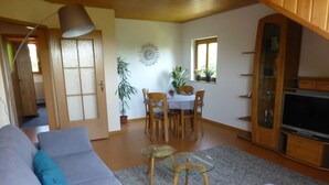 Una sala de estar con sofá, una mesa de centro de vidrio, una mesa de comedor con sillas y un mueble para televisión.
