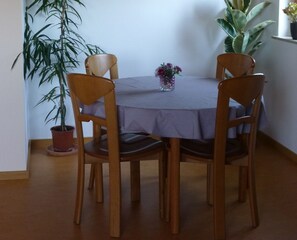Ruokapöytä, jossa on neljä puista tuolia, ruukkukasvi ja maljakko kukkineen.