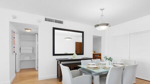 A dining area with a glass table, white chairs, a large mirror, and a ceiling light fixture. - Beautiful Apartment with Pool & Amenities (Hollywood)