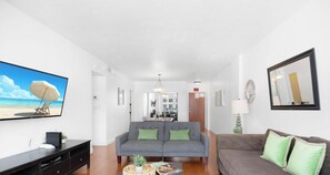 A living room with a sofa, a coffee table, and a TV displaying a beach scene.