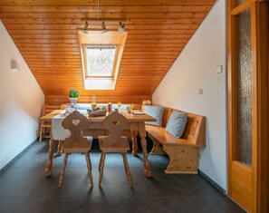 Une pièce chaleureuse avec un plafond en bois, une lucarne, une table à manger avec des chaises, un banc et une petite fenêtre.