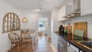 A kitchen with wooden chairs, a dining table, a coffee machine, and a cutting board.