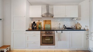 A kitchen with white cabinets, a stainless steel oven, a wooden cutting board, and a sink.