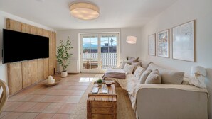 A living room with a flat-screen TV, wooden panel wall, sofa, and a large window with a view.