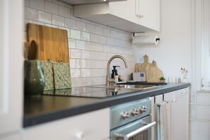 A modern kitchen with white cabinets, a black countertop, a stainless steel sink, and a wooden cutting board.