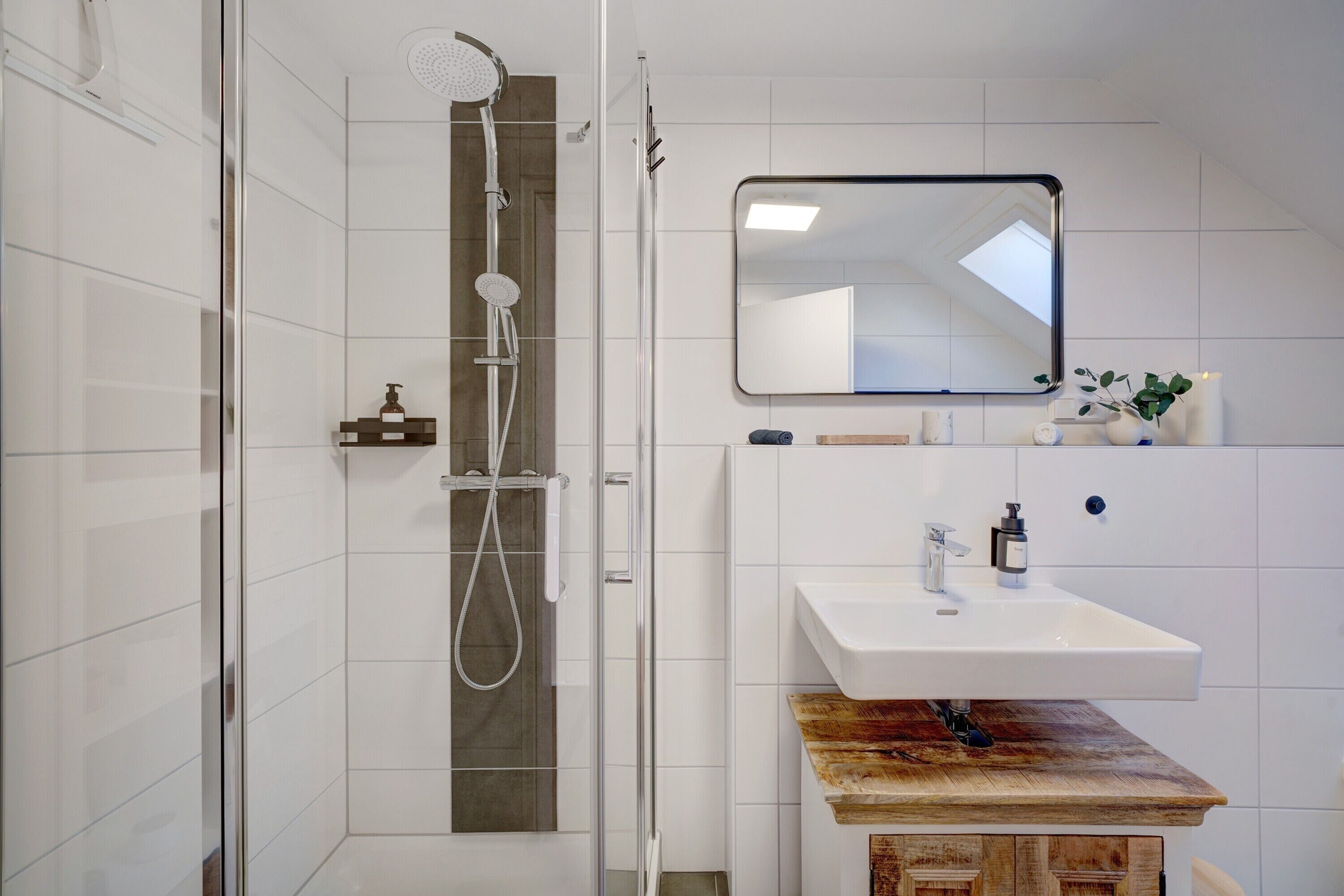 Une salle de bain moderne dotée d’une douche à parois de verre, d’un meuble-lavabo en bois et d’un miroir placé au-dessus du meuble-lavabo.