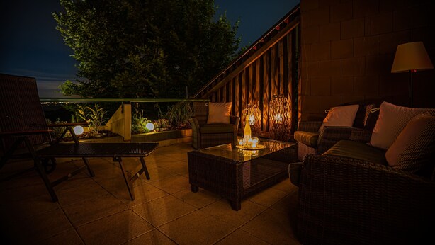 An outdoor patio area with wicker furniture, a glass-top table, and ambient lighting. - Apartment 'Natur Tanken' with Mountain View, Shared Garden and Wi-Fi (Sasbachwalden)