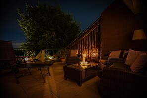 Un espace extérieur aménagé en terrasse, avec des meubles en osier, une table à plateau en verre et un éclairage d’ambiance.