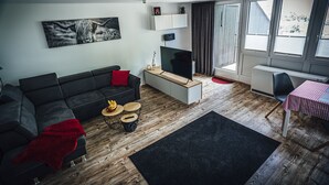 A modern living room with a black sofa, a red throw blanket, a wooden coffee table, and a flat-screen TV. - Apartment 'Natur Tanken' with Mountain View, Shared Garden and Wi-Fi (Sasbachwalden)