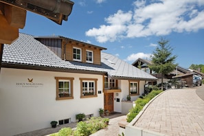 A residential building with a tiled roof, wooden balconies, and a paved driveway.