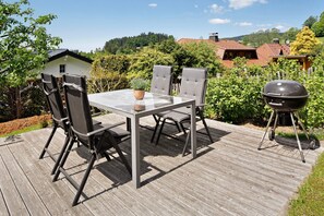 Eine Terrasse im Freien mit Tisch, Stühlen, einem Grill und einem Haus im Hintergrund.