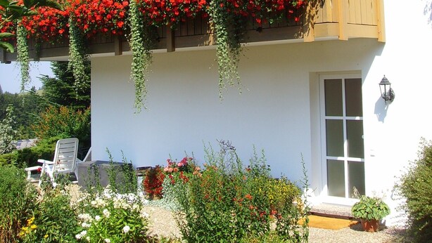A two-story building with multiple balconies adorned with red flowers.