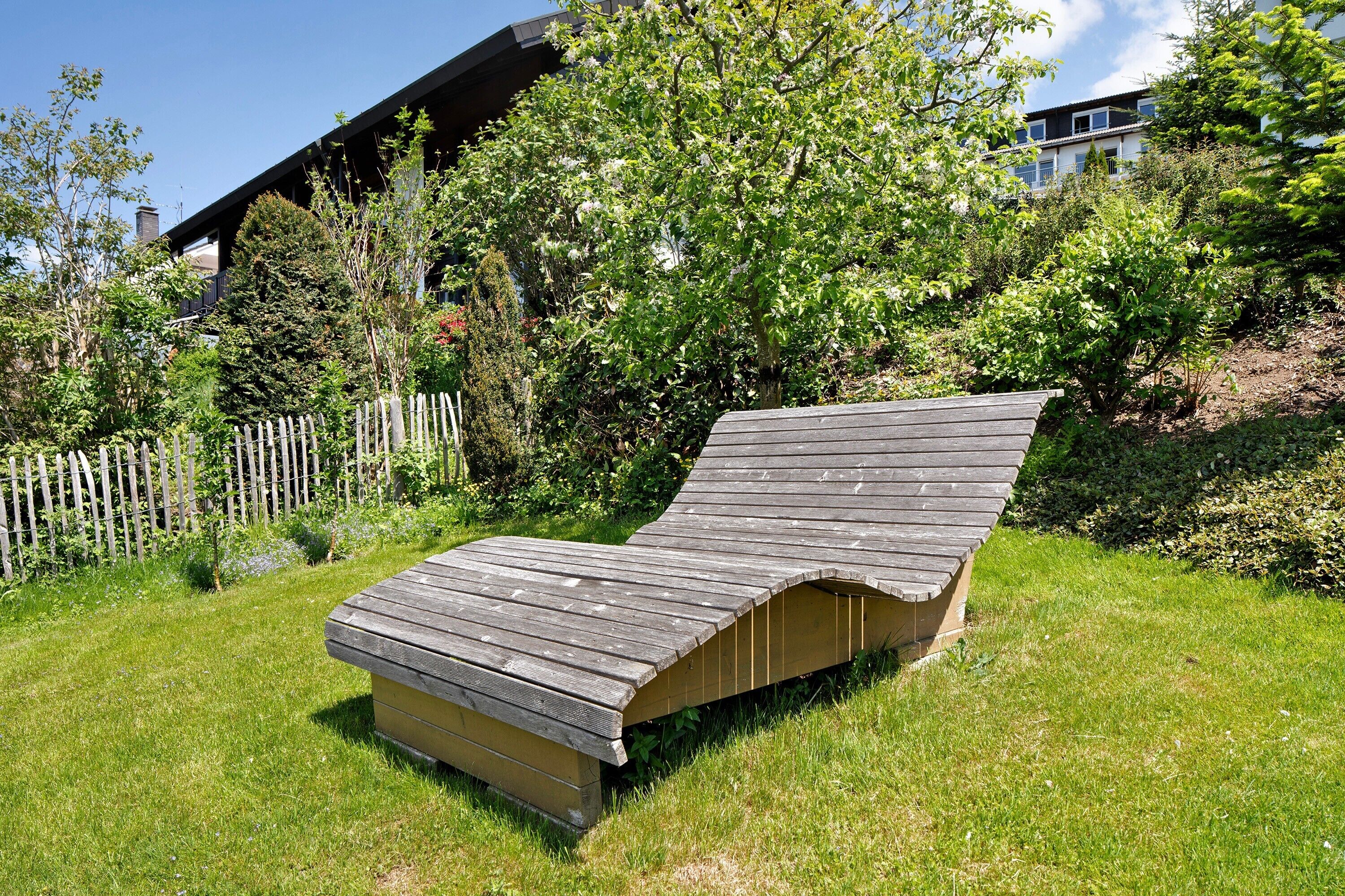 A wooden deck with a curved roof, surrounded by a grassy area and trees.