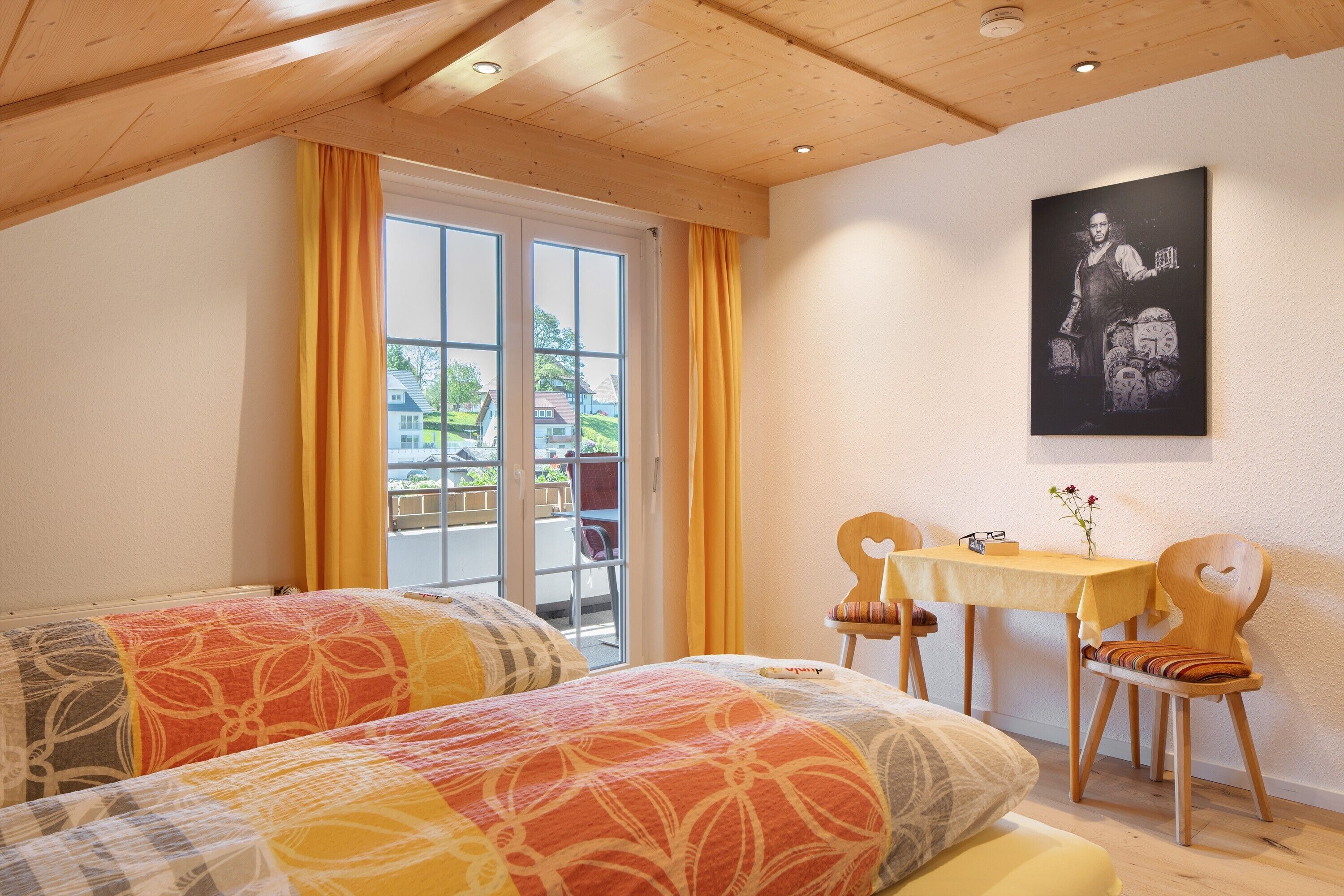 A bedroom with two beds, a table with chairs, a painting on the wall, and a window with curtains.