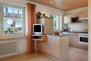 Et moderne køkken med en indbygget ø, mikroovn, ovn og et vindue med udsigt til en balkon.