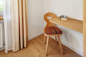 Une chaise en bois avec un dossier en forme de cœur et un coussin à rayures, placée à côté d’une étagère en bois sur laquelle repose une paire de lunettes.